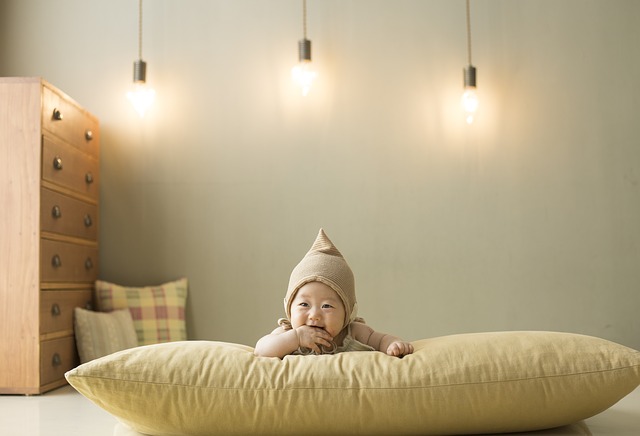 Malý Číňan v béžové čepici leží na velkém béžovém polštáři, za ním svítí tři žárovky